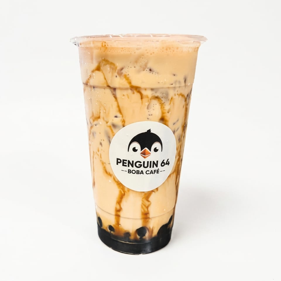 Caramel milk tea with tapioca pearls in a branded Penguin 64 Boba Café cup.